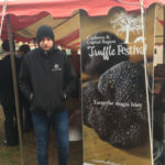 Ganymede Truffles Lachie looking cold standing next to a banner reading Canberra Truffle Festival Taste the Magic here